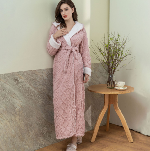 Frau in rosa Bademantel aus Fleece, stehend neben Tisch mit Teetasse und Vase, gemütliche Kleidung.