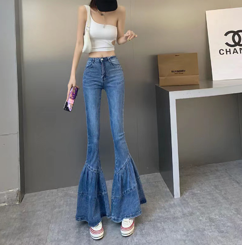 Frau in Schlagjeans und weißem Top, hält Smartphone, modisch, urbaner Stil.
