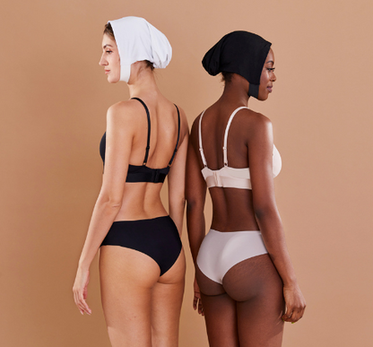 Zwei Frauen in nahtloser Unterwäsche, schwarz und beige, mit Kopftüchern, Rückansicht.