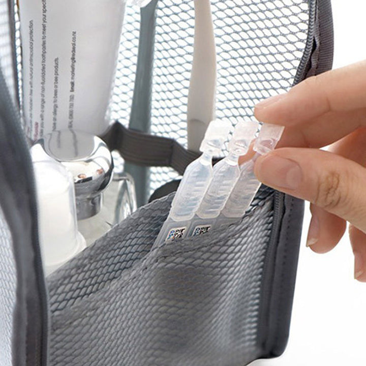 Nahaufnahme der grauen Netztasche von innen, eine Hand zieht kleine Ampullen aus dem Netzfach, dahinter Tube und Flaschen. 3