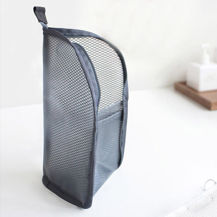Graue Netztasche steht aufrecht auf einer weißen Fläche, mit Tragschlaufe oben und Außenfach an der Seite. 7