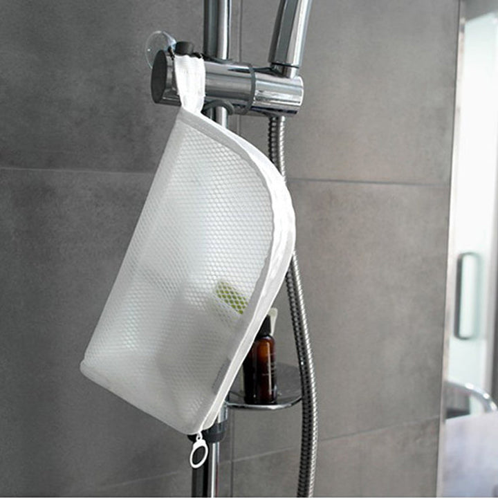 Weiße Netztasche hängt mit einer Schlaufe an der Duschstange in einer grau gefliesten Dusche, darunter eine braune Flasche. 4