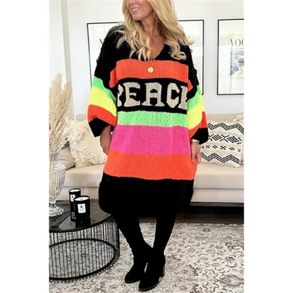 Frau trägt bunten Strickcardigan mit "PEACE"-Aufdruck, Regenbogenfarben, gemütlich, modisch.