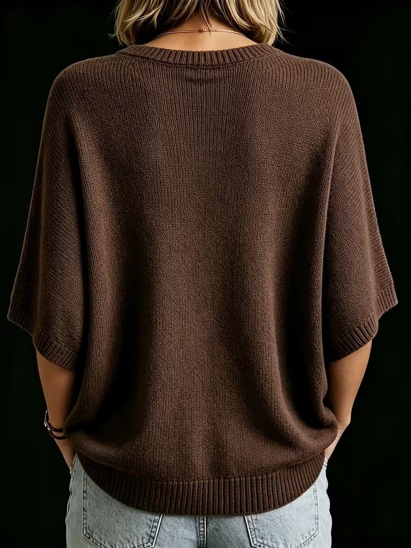 Rückansicht des braunen Strickoberteils mit Fledermausärmeln und gerippten Bündchen, getragen zu heller Jeans, Hände in den Hosentaschen. 21