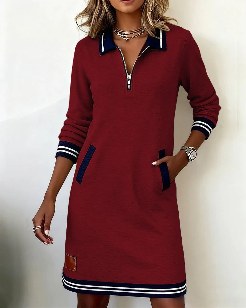 Weinrotes Kleid mit dunkelblauem Kragen, Taschenpaspeln und gestreiften Ärmelbündchen, getragen von einer Frau mit Hand in der Tasche. 5