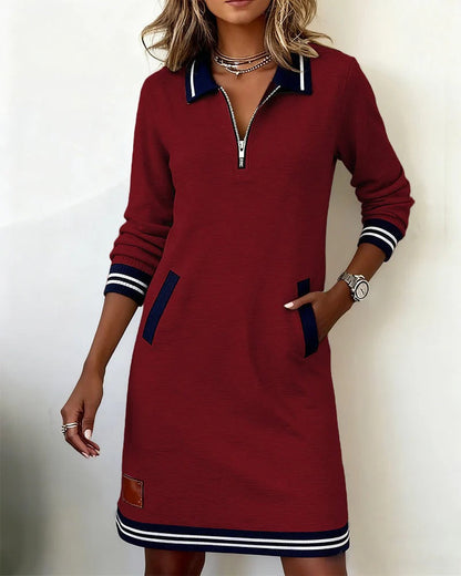 Weinrotes Kleid mit dunkelblauem Kragen, Taschenpaspeln und gestreiften Ärmelbündchen, getragen von einer Frau mit Hand in der Tasche. 5