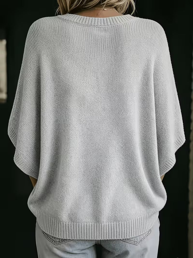 Rückansicht des hellgrauen Strickoberteils mit Rundhalsausschnitt, gerippten Ärmelbündchen und breitem Saum, getragen mit heller Jeans. 3