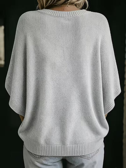 Rückansicht des hellgrauen Strickoberteils mit Rundhalsausschnitt, gerippten Ärmelbündchen und breitem Saum, getragen mit heller Jeans. 3
