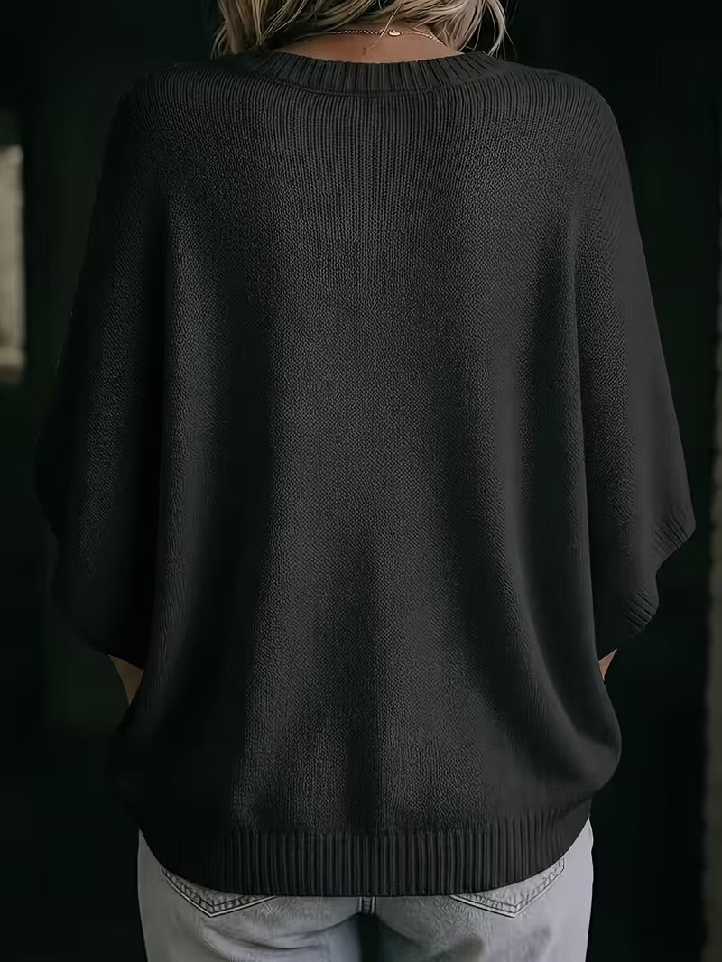 Rückansicht des schwarzen Strickoberteils mit Rundhalsausschnitt, weiten Fledermausärmeln und gerippten Bündchen, getragen zu heller Jeans. 28