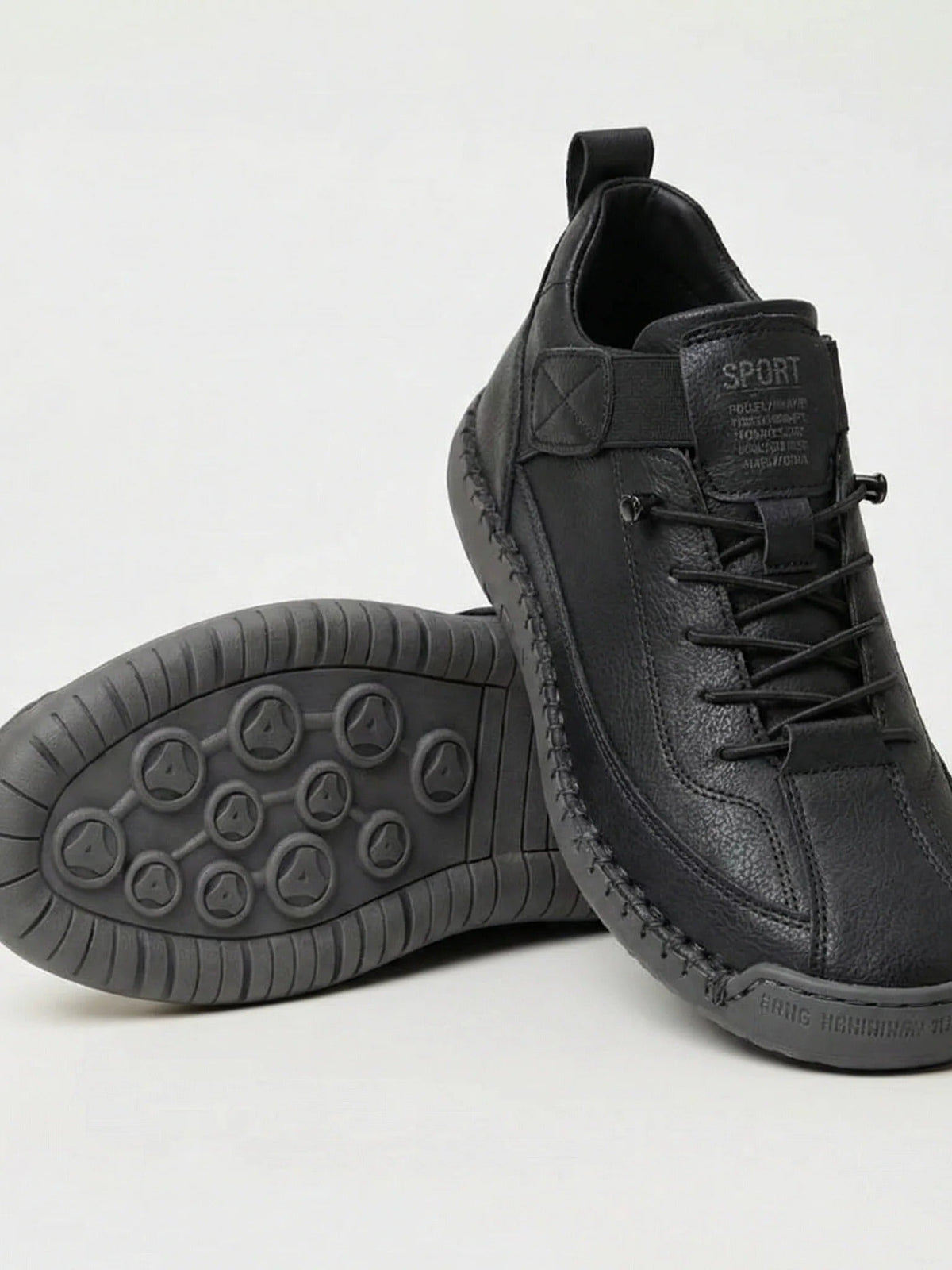 Schwarze Sneaker, ein Schuh seitlich aufgestellt, der andere zeigt die graue Profilsohle mit runden Noppen 1