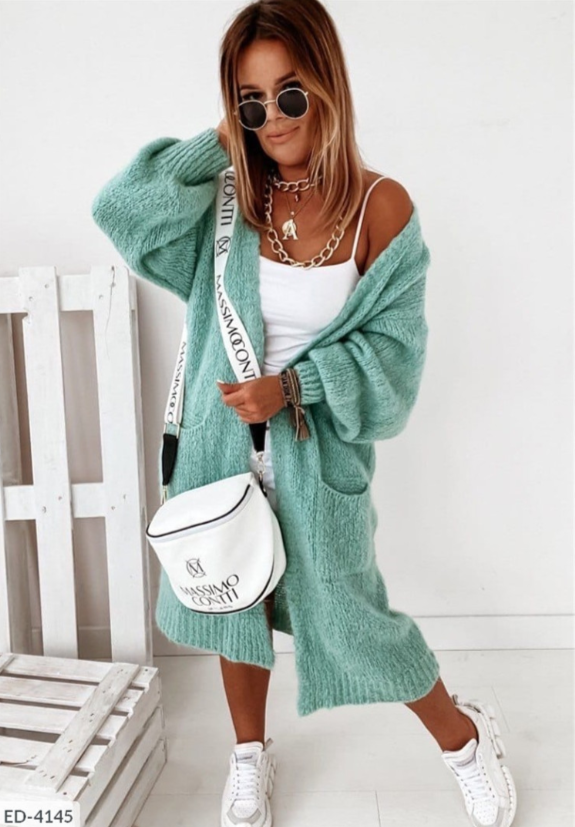 Frau in mintgrünem Strickcardigan, weißem Top, Sonnenbrille, mit weißer Umhängetasche.