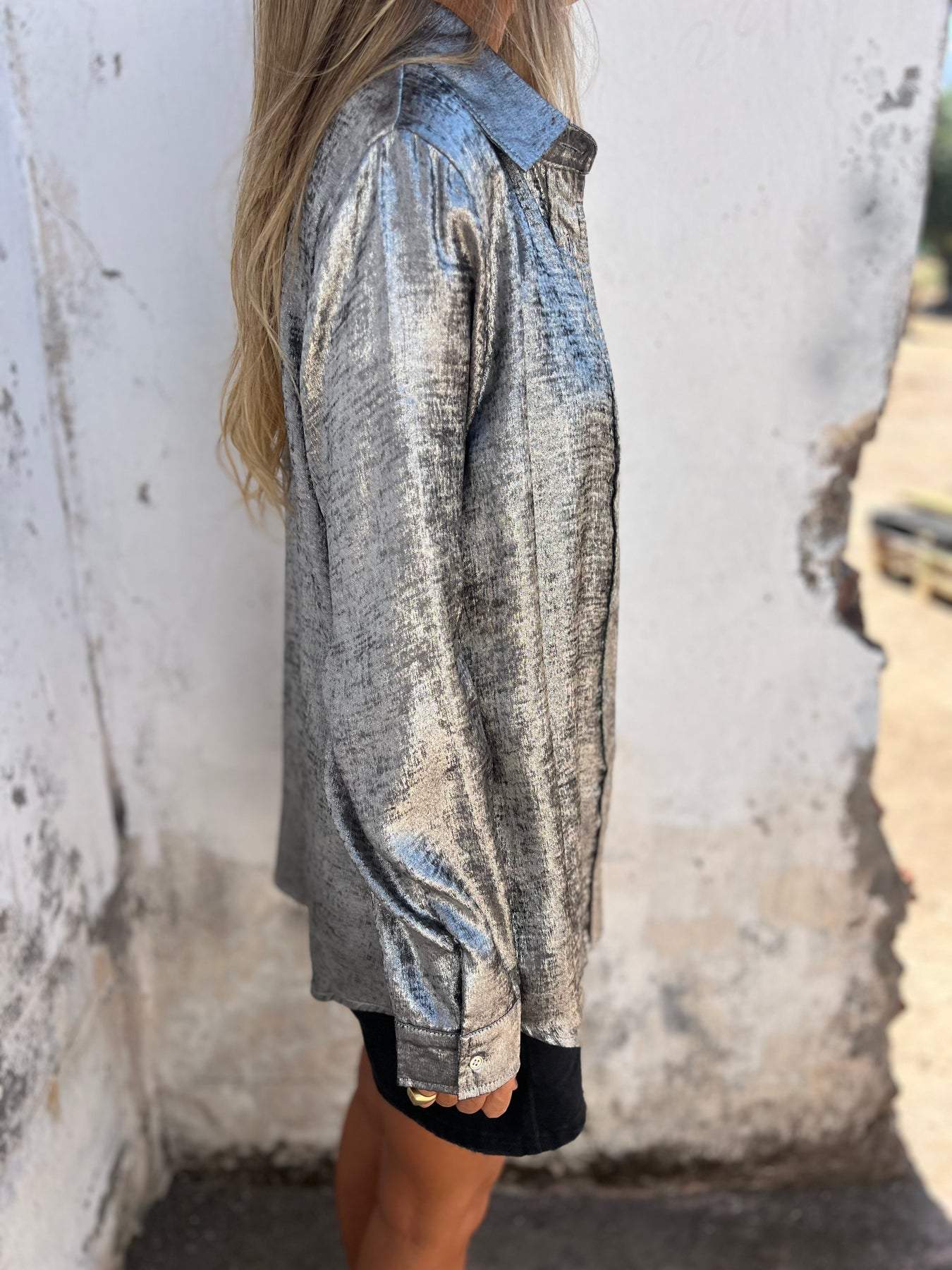 Frau in silberner Metallic-Bluse, seitlich, vor weißer Wand, modisch, elegant, glänzend.