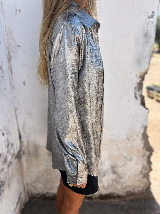 Frau in silberner Metallic-Bluse, seitlich, vor weißer Wand, modisch, elegant, glänzend.