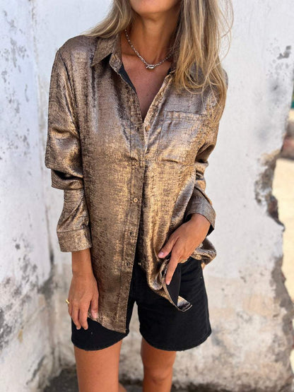 Frau in glänzender, goldener Bluse und schwarzen Shorts vor weißer Wand.