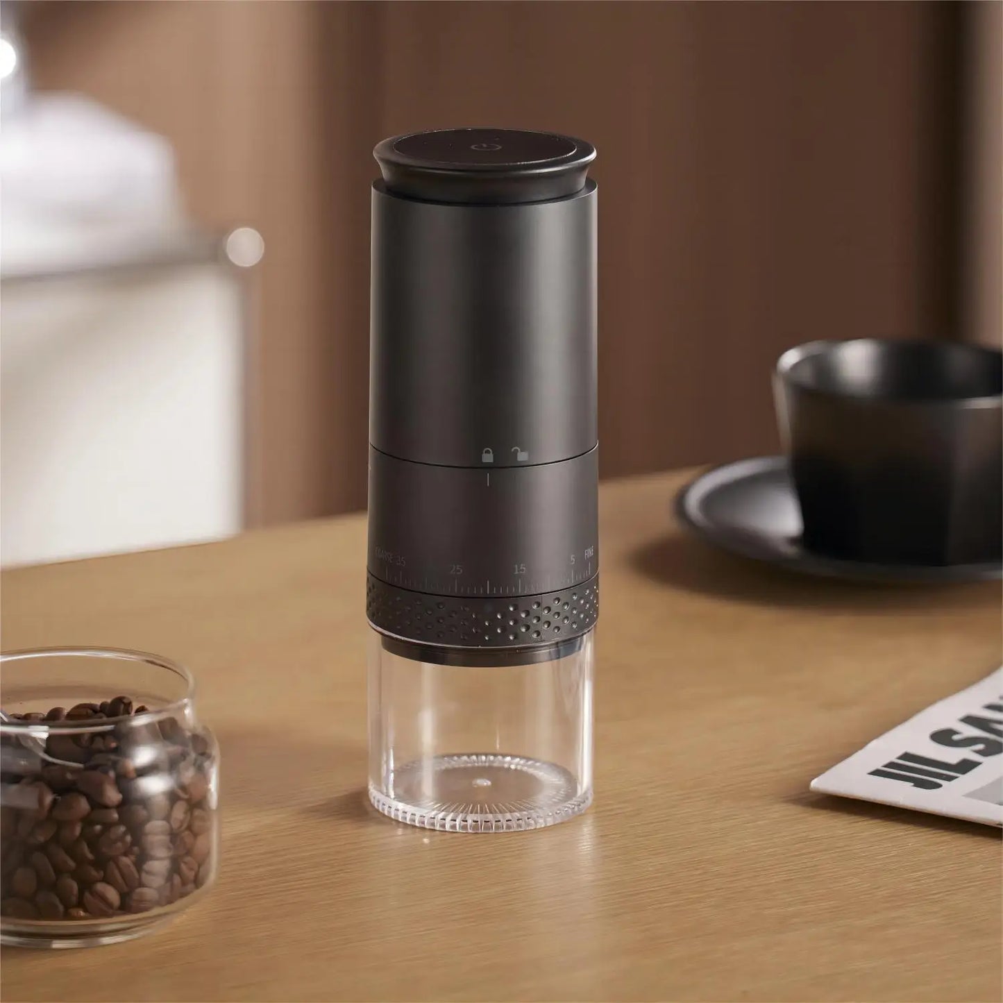 Schwarze Kaffeemühle aus Edelstahl auf Holztisch neben Kaffeebohnen und Tasse.