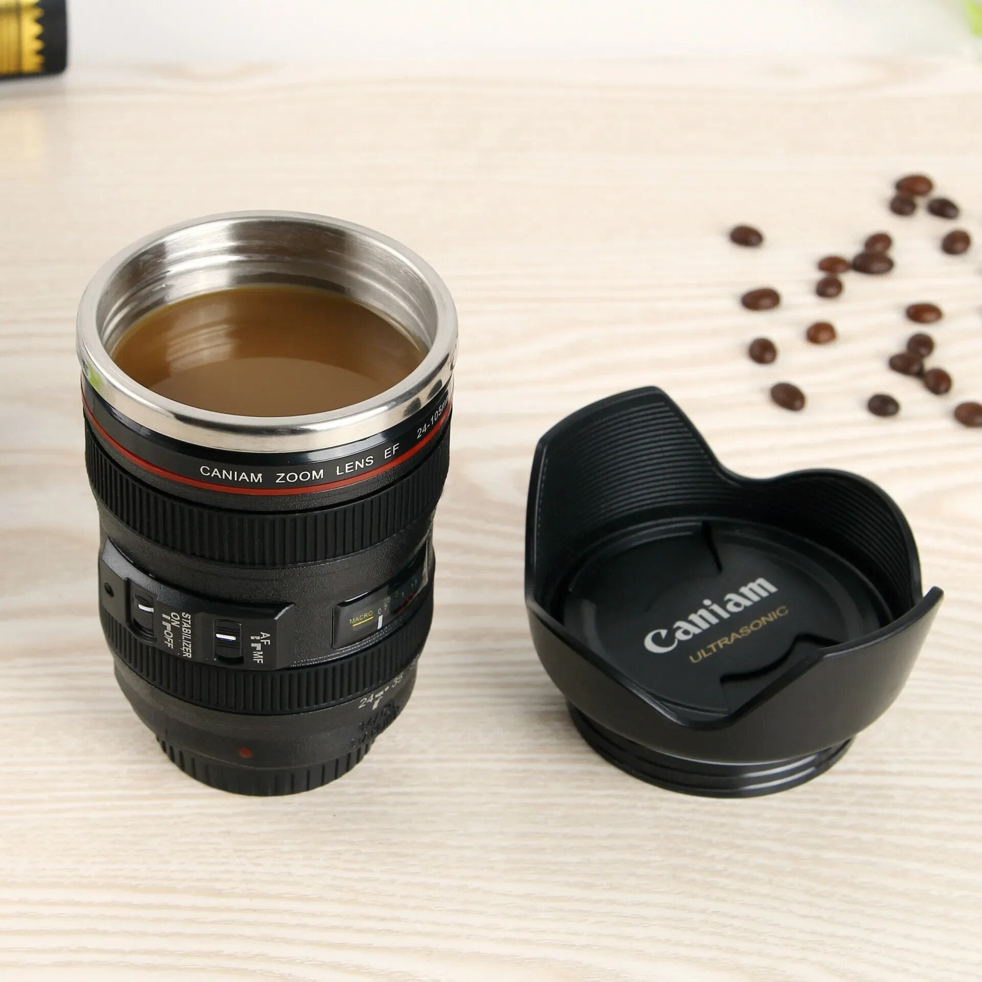Kaffeetasse in Kameraobjektiv-Design, schwarz, Edelstahl, mit Deckel, auf Holztisch.