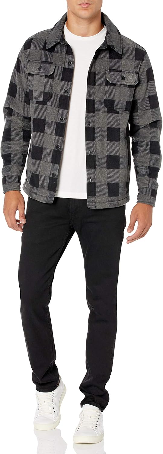 Mann in schwarz-grauer Karo-Jacke, weißem T-Shirt, schwarzer Hose und weißen Sneakers.