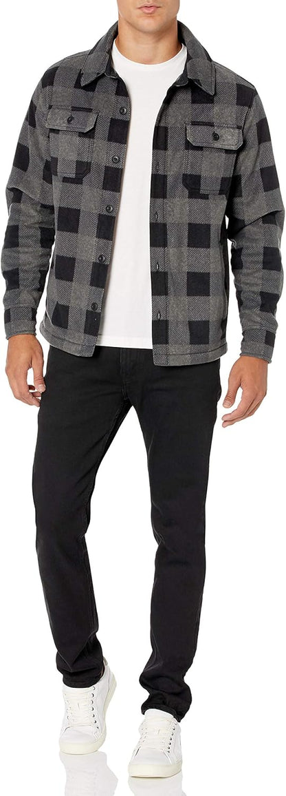 Mann in schwarz-grauer Karo-Jacke, weißem T-Shirt, schwarzer Hose und weißen Sneakers.