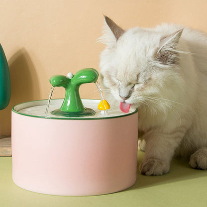 Weiße Katze trinkt aus rosa Katzenbrunnen mit grünem Sprinkler, Haustierbedarf, Trinkbrunnen.