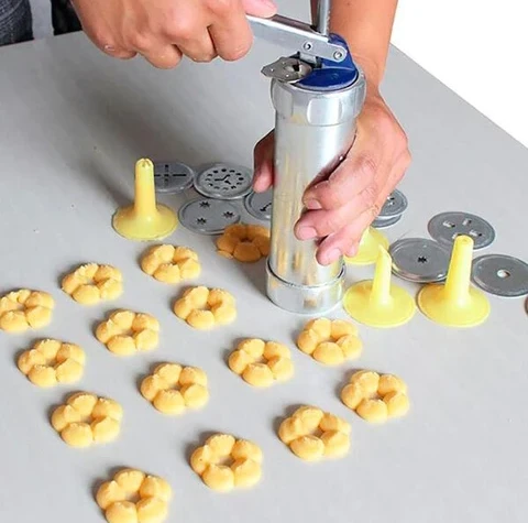 Person verwendet Keksstempel aus Metall mit gelben Aufsätzen, um Blumenplätzchen zu formen.