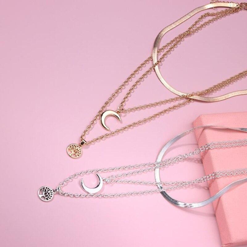 Goldene und silberne Halsketten mit Halbmond und Lebensbaum auf rosa Hintergrund.
