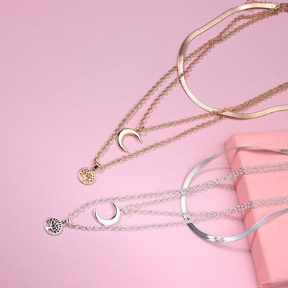 Goldene und silberne Halsketten mit Halbmond und Lebensbaum auf rosa Hintergrund.