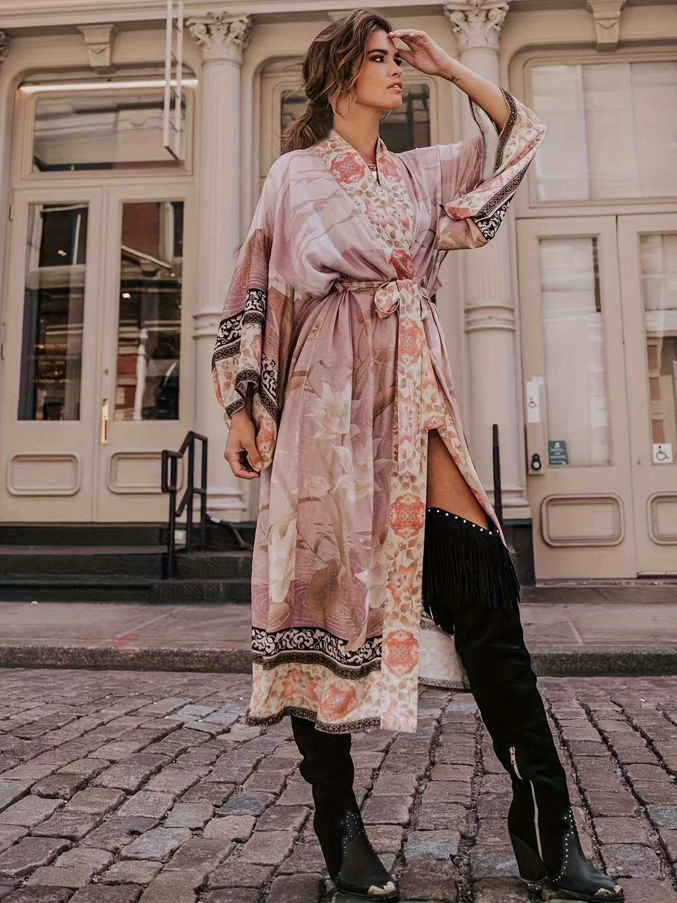 Frau in rosa Kimono mit Blumenmuster und schwarzen Stiefeln auf Kopfsteinpflaster vor Gebäude.