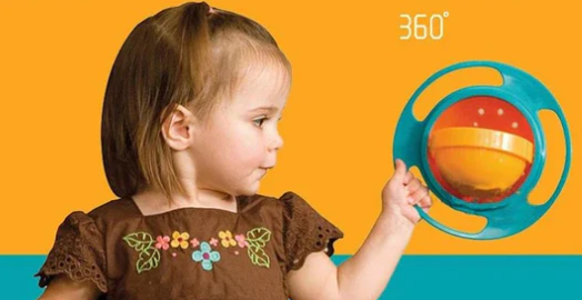 Kleinkind mit blauem 360° Gyroskop-Schüsselspielzeug, orangefarbene Schüssel, gelber Hintergrund.