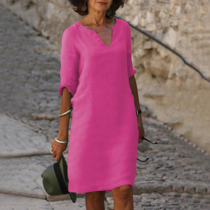 Frau in pinkem Sommerkleid, V-Ausschnitt, auf Kopfsteinpflasterweg, modisch, elegant.