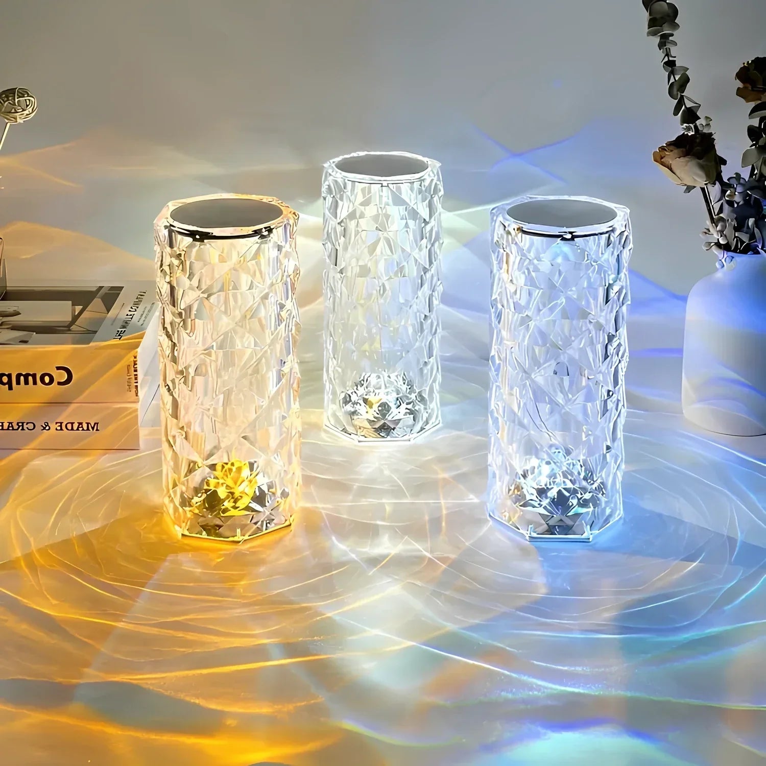 Drei LED-Kristalllampen, farbwechselnd, auf Tisch mit Blumen und Buch, moderne Dekoration.