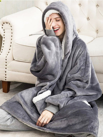 Frau in grauem, flauschigem Oversize-Kapuzenpullover auf Sofa, gemütliche Winterkleidung.