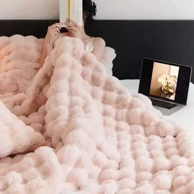 Flauschige rosa Decke auf Bett, Person liest Buch, Laptop mit Blumenbild, gemütliches Schlafzimmer.