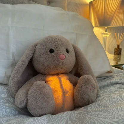 Plüsch-Hase mit leuchtendem Bauch, sensorisches Spielzeug, beige, auf Bett, beruhigend für Babys.