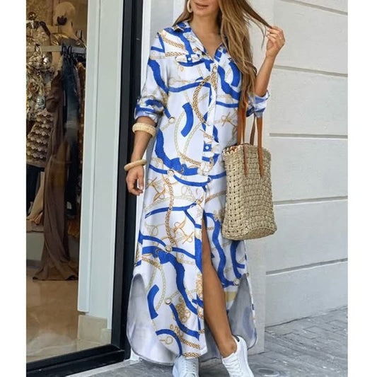 Frau in langem, gemustertem Hemdkleid mit blau-weißen Kettenmotiven, Strohtasche, weiße Sneaker.