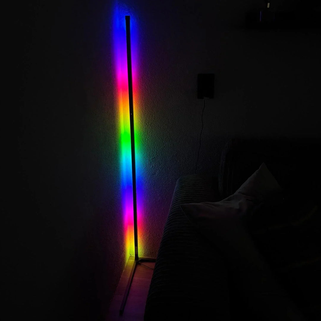 Eckstehlampe im dunklen Raum mit farbigem Lichtverlauf von Blau über Grün bis Pink, daneben Sofa mit Kissen. 6