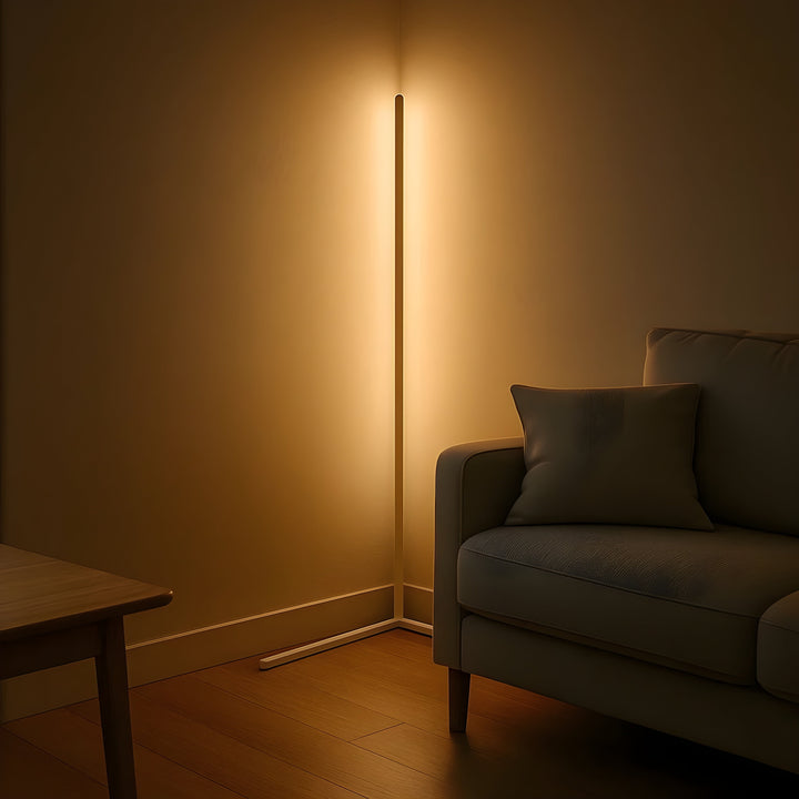 Weiße Eckstehlampe leuchtet warm in der Zimmerecke neben einem Sofa mit Kissen und einem Holztisch. 7