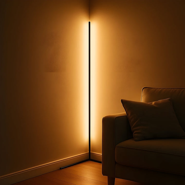 Schwarze Eckstehlampe taucht die Wand in warmes, goldenes Licht, rechts im Bild ein Sofa mit Kissen. 3