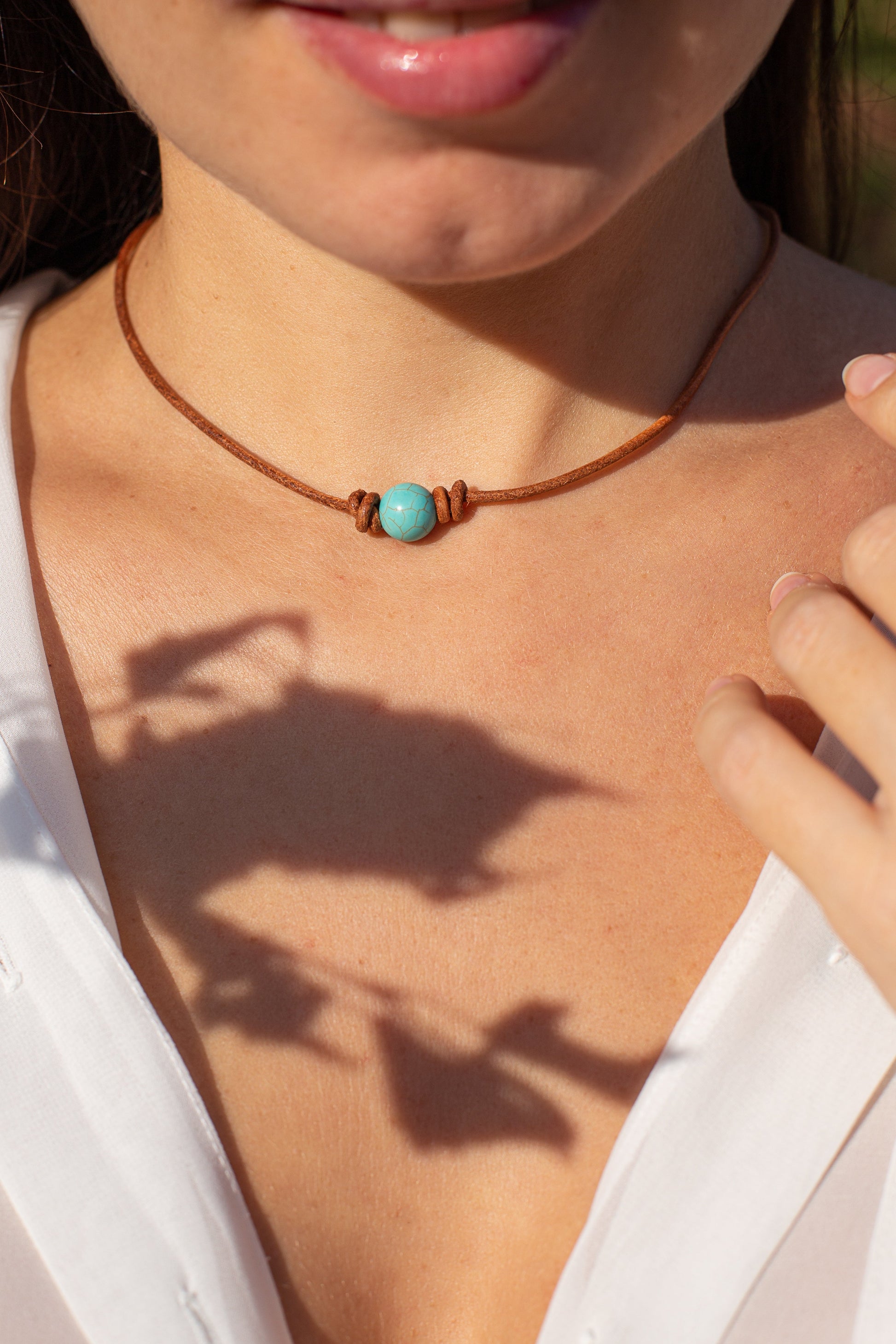 Frau mit braunem Lederhalsband und türkisfarbenem Stein, Nahaufnahme, modisches Accessoire.