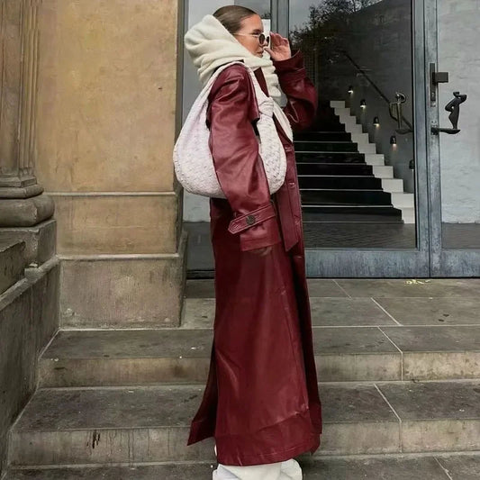 Frau in rotem Ledermantel mit weißer Handtasche und Sonnenbrille auf Treppe.