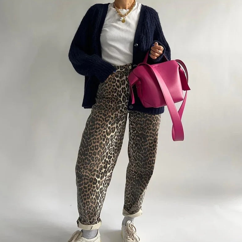 Frau mit Leopardenhose, schwarzer Strickjacke, weißem T-Shirt und pinker Tasche.