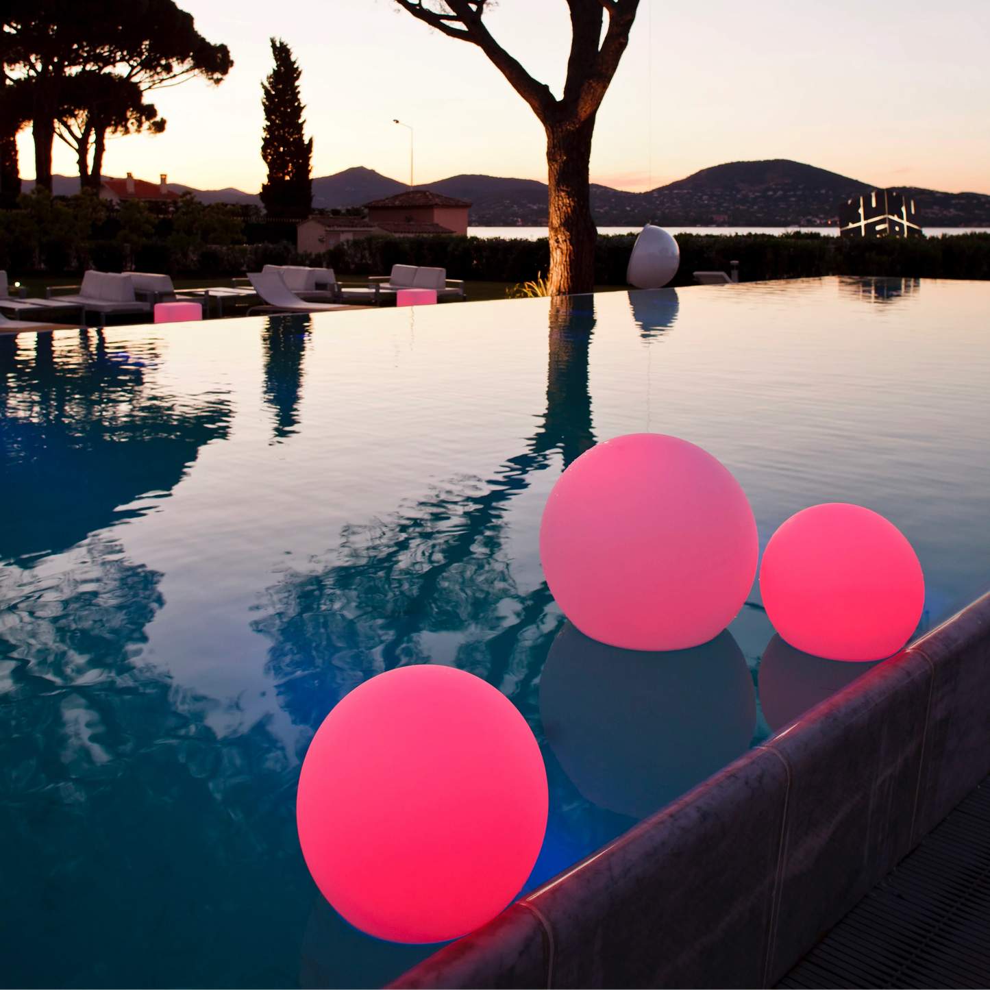 Leuchtende rosa Kugeln im Pool bei Sonnenuntergang, moderne Gartenbeleuchtung, Außenbereich.