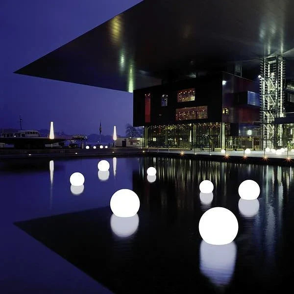 Leuchtende Kugeln auf Wasser vor modernem Gebäude bei Nacht, Architektur, Beleuchtung, Stadtbild.