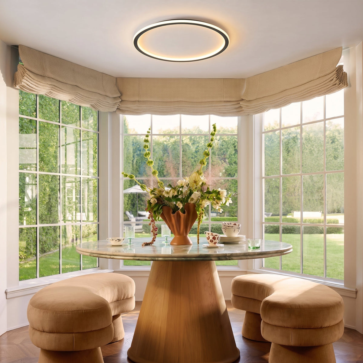 Leuchtender Lichtring über einem runden Esstisch in einem Erker mit großen Sprossenfenstern und gepolsterten Sitzbänken. 7