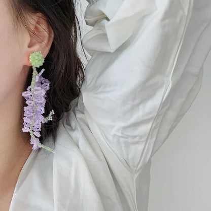 Frau mit handgefertigtem Ohrring aus lila und grünem Perlen, elegantes Schmuckdesign.