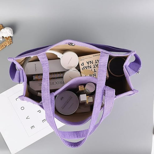 Lila Stofftasche mit Kosmetikprodukten, Büchern und Accessoires, ideal für Reisen und Alltag.