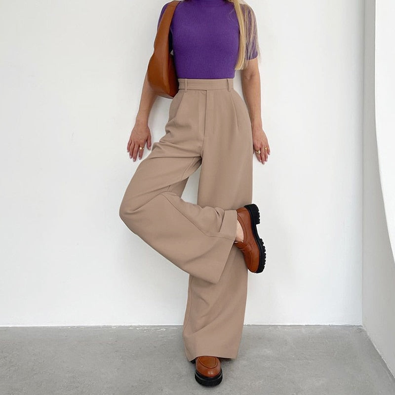 Frau in lila Oberteil und beigen Schlaghosen, braune Schuhe, modisch, elegant, minimalistisch.