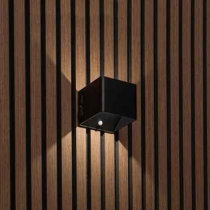 Schwarze würfelförmige Wandleuchte an Holzlamellenwand, Seitenansicht mit Schalter und Bewegungssensor an der Unterseite 1