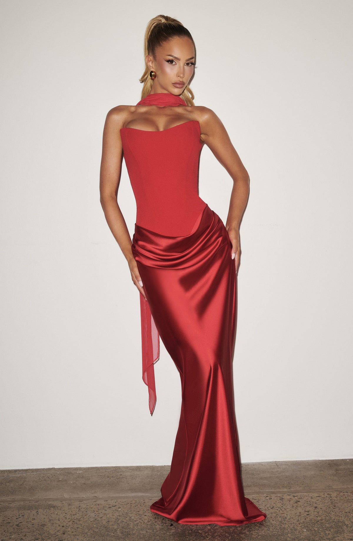 Rotes Korsettkleid mit Chiffonschal, Model mit hohem Zopf vor heller Wand, Hand an der Hüfte 14