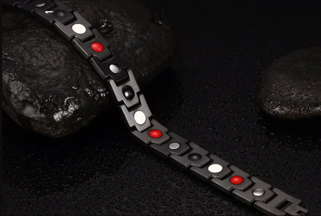 Schwarzes magnetisches Armband mit roten und weißen Elementen auf nassem Stein.