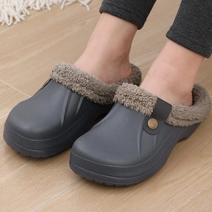 Nahaufnahme der Füße in grauen Clogs mit Fellfutter und Riemen mit Knopf auf hellem Holzboden. 8
